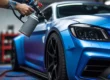 Close-up de um profissional aplicando envelopamento líquido (Plasti Dip) com uma pistola de pintura em um carro esportivo, mostrando a transição da cor original para um acabamento azul fosco, simbolizando a customização automotiva.