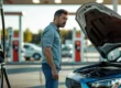 Motorista preocupado ao lado de um carro com o capô aberto em um posto de gasolina após abastecer e o motor falhar.