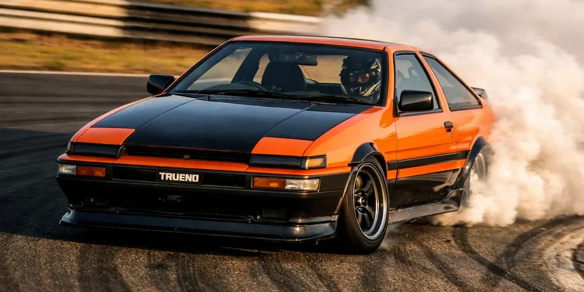 Carro de drift em curva com fumaça saindo dos pneus traseiros evidenciando o desgaste de borracha em pista.