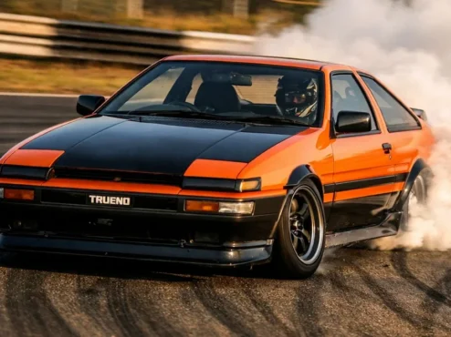 Carro de drift em curva com fumaça saindo dos pneus traseiros evidenciando o desgaste de borracha em pista.