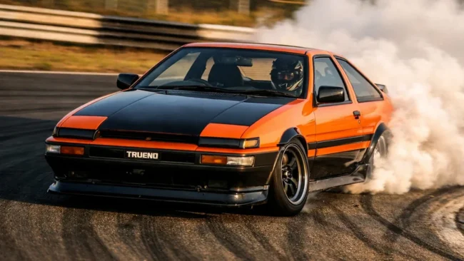 Carro de drift em curva com fumaça saindo dos pneus traseiros evidenciando o desgaste de borracha em pista.