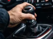 Close-up de mão de motorista trocando marcha, ilustrando hábitos que podem afetar a transmissão do veículo.