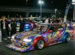 Um carro estilo Kaido Racer japonês com escapamentos Takeyari altos e pintura colorida em um encontro noturno no Japão.