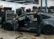 Carro elétrico modificado em uma oficina de alta performance com laptops conectados para ajuste de software e suspensão a ar.