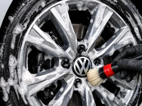 Profissional aplicando pincel de detalhamento em roda de liga leve com espuma de shampoo neutro para limpeza segura.