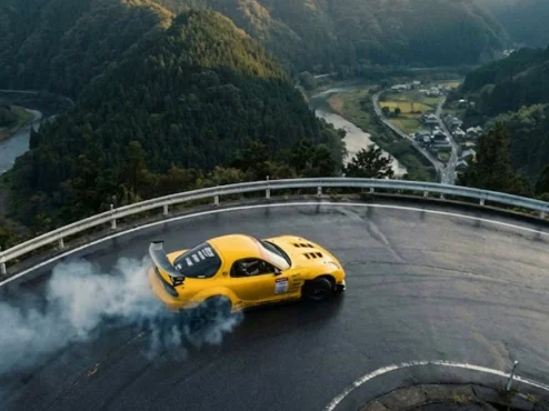 Mazda RX7 amarelo executando um drift perfeito em estrada sinuosa