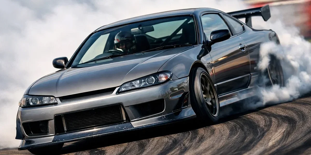 nissan-silvia-s15-drift-curva-tracao-traseira Um Nissan Silvia S15 realizando uma manobra de drift em pista, destacando a inclinação da carroceria e a fumaça nos pneus traseiros.