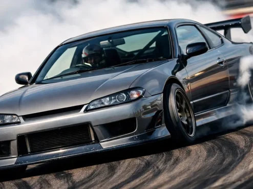 Um Nissan Silvia S15 realizando uma manobra de drift em pista, destacando a inclinação da carroceria e a fumaça nos pneus traseiros.