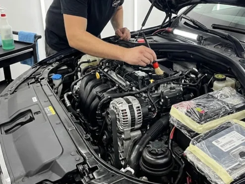 Profissional realizando detalhamento de cofre de motor com pincel e proteção em componentes eletrônicos.