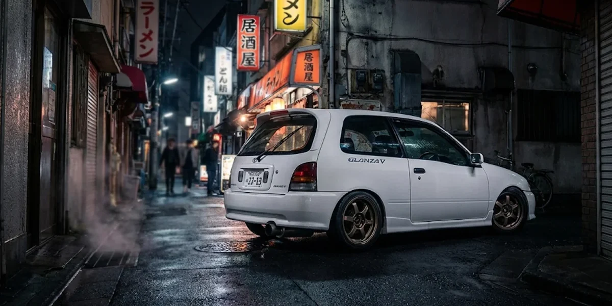 toyota-starlet-glanza-v-ep91-jdm-tuning Toyota Starlet Glanza V branco rebaixado com rodas de liga leve em um cenário urbano japonês à noite.