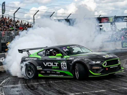 drift-eletrico-competicao-torque-pneus Carro de drift elétrico de alta performance em ângulo acentuado soltando fumaça densa dos pneus em uma pista de asfalto.