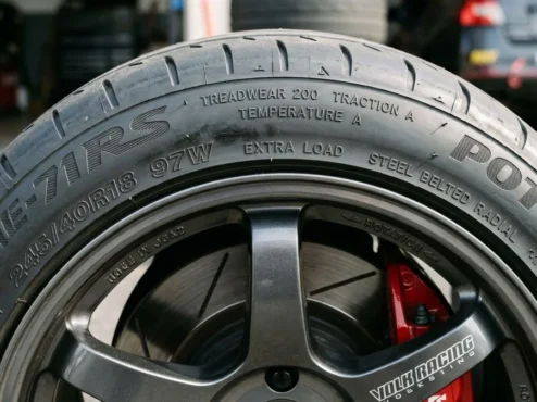 guia-utqg-treadwear-traction-temperature-pneu Lateral de um pneu de alta performance mostrando os índices de Treadwear, Traction e Temperature gravados na borracha.