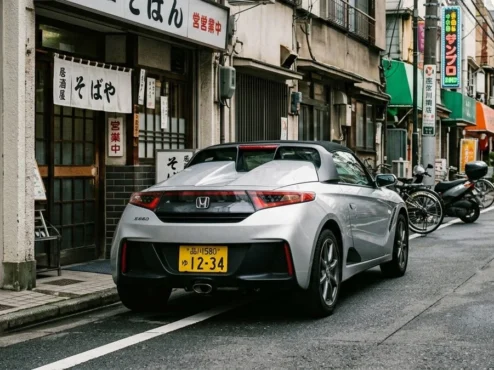 honda-s660-placa-amarela-rua-toquio-jdm Um esportivo Honda S660 prata estacionado em uma rua de Tóquio, exibindo a característica placa amarela dos Kei Cars.