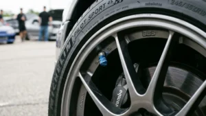 Detalhe de uma roda esportiva com tampa de válvula em alumínio azul, destacando a manutenção preventiva e estética automotiva.