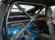 Detalhe de uma meia-gaiola (roll bar) instalada em um carro esportivo, mostrando a ancoragem e a proximidade com os bancos.