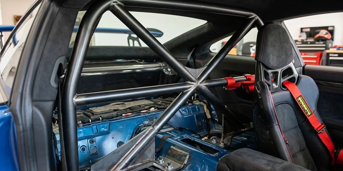 Detalhe de uma meia-gaiola (roll bar) instalada em um carro esportivo, mostrando a ancoragem e a proximidade com os bancos.