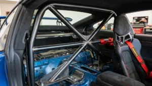 Detalhe de uma meia-gaiola (roll bar) instalada em um carro esportivo, mostrando a ancoragem e a proximidade com os bancos.