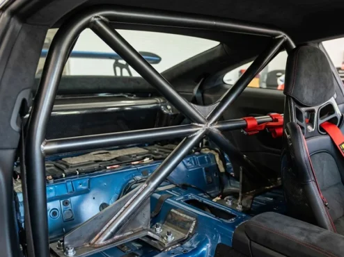 instalacao-roll-bar-carro-rua-seguranca Detalhe de uma meia-gaiola (roll bar) instalada em um carro esportivo, mostrando a ancoragem e a proximidade com os bancos.