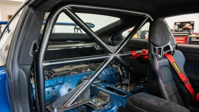 Detalhe de uma meia-gaiola (roll bar) instalada em um carro esportivo, mostrando a ancoragem e a proximidade com os bancos.