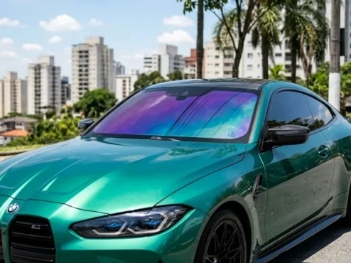Carro esportivo com película camaleão no parabrisa apresentando variações de tons roxo e azul sob a luz solar.