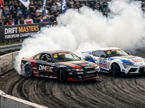 Dois carros de drift profissionais em uma batalha de proximidade extrema no Drift Masters, gerando muita fumaça em uma curva fechada.