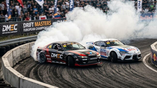 Dois carros de drift profissionais em uma batalha de proximidade extrema no Drift Masters, gerando muita fumaça em uma curva fechada.