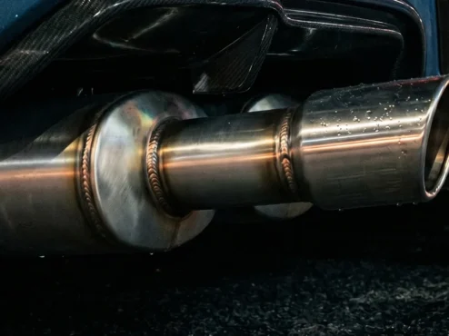 Close-up de uma ponteira de escapamento esportivo em inox em um carro customizado durante a noite.