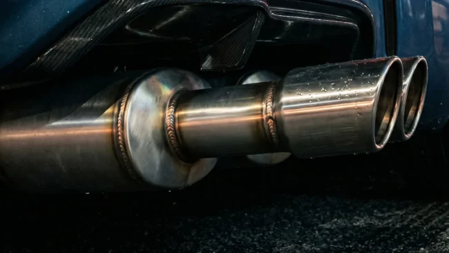 Close-up de uma ponteira de escapamento esportivo em inox em um carro customizado durante a noite.