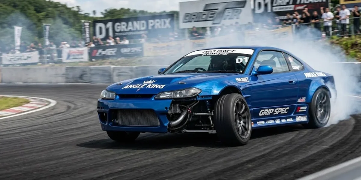 Carro de tração traseira em drift de alto ângulo, exibindo a roda dianteira esterçada através de um angle kit profissional.