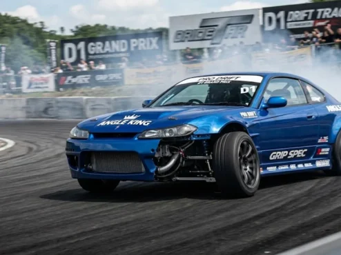 Carro de tração traseira em drift de alto ângulo, exibindo a roda dianteira esterçada através de um angle kit profissional.