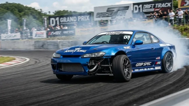 Carro de tração traseira em drift de alto ângulo, exibindo a roda dianteira esterçada através de um angle kit profissional.