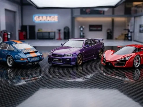Três miniaturas detalhadas em escala 1/64 sobre base de fibra de carbono, representando a tendência diecast de 2026