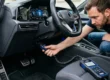 Homem conectando um scanner OBD2 na porta de diagnóstico sob o painel de um carro moderno.
