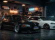 Dois Honda Civic estilo stance e JDM em uma garagem escura, com destaque para a placa de coleção no veículo customizado.