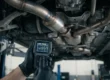 Mecânico utilizando scanner OBD2 para diagnosticar o código de erro P0420 no sistema de exaustão de um carro.