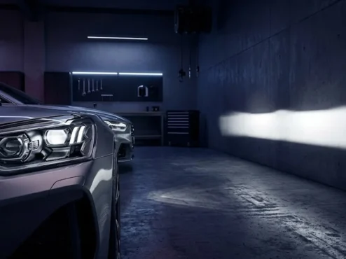 farol-carro-customizado-linha-de-corte-legalizada Farol esportivo automotivo com lente projetora exibindo uma linha de corte de luz perfeita contra uma parede escura.
