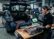 Mecânico com luvas de proteção inspecionando módulos elétricos da bateria de tração de um carro híbrido em uma oficina especializada.