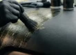Detalhador automotivo removendo resíduo brilhante de silicone de um painel texturizado com pincel macio.