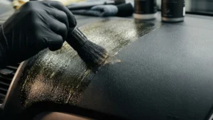 Detalhador automotivo removendo resíduo brilhante de silicone de um painel texturizado com pincel macio.
