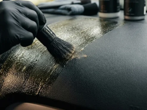 Detalhador automotivo removendo resíduo brilhante de silicone de um painel texturizado com pincel macio.