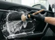 Detalhador automotivo utilizando pincel macio de detalhamento e espuma de APC automotivo para limpar profundamente o painel de plástico texturizado de um veículo.