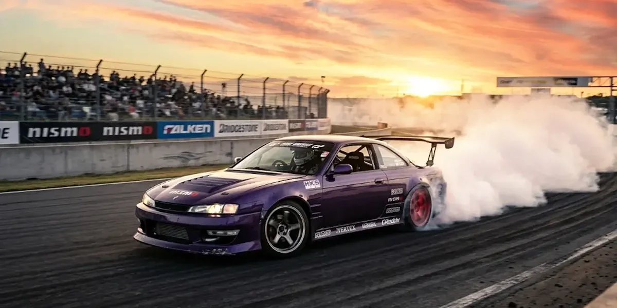 Carro japonês clássico Nissan Silvia modificado realizando manobra de drift em pista com muita fumaça nos pneus.