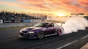 Carro japonês clássico Nissan Silvia modificado realizando manobra de drift em pista com muita fumaça nos pneus.