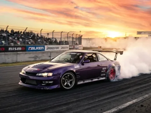 Carro japonês clássico Nissan Silvia modificado realizando manobra de drift em pista com muita fumaça nos pneus.