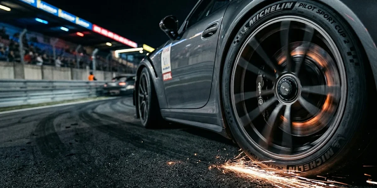 Detalhe de pneu esportivo em alta velocidade em pista de corrida à noite, evidenciando o estresse térmico do composto de borracha.