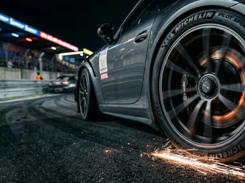 Detalhe de pneu esportivo em alta velocidade em pista de corrida à noite, evidenciando o estresse térmico do composto de borracha.