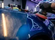 Polimento técnico profissional em para-lama de carro esportivo azul metálico com politriz orbital em estúdio de detalhamento.