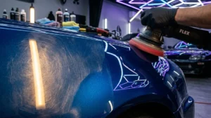 Polimento técnico profissional em para-lama de carro esportivo azul metálico com politriz orbital em estúdio de detalhamento.