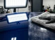 Mão com luva preta passando pano de microfibra em pintura automotiva sob luz de inspeção mostrando reflexos e riscos.