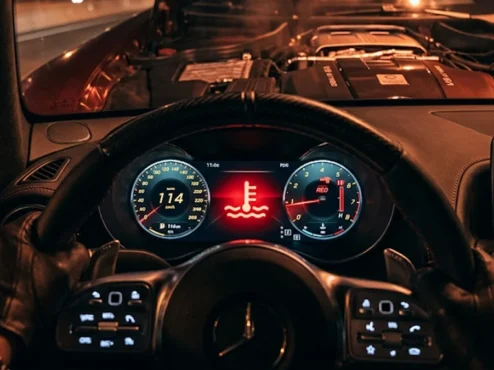 Foto detalhada do painel de instrumentos de um carro focado na luz vermelha de alerta de temperatura do motor acesa.